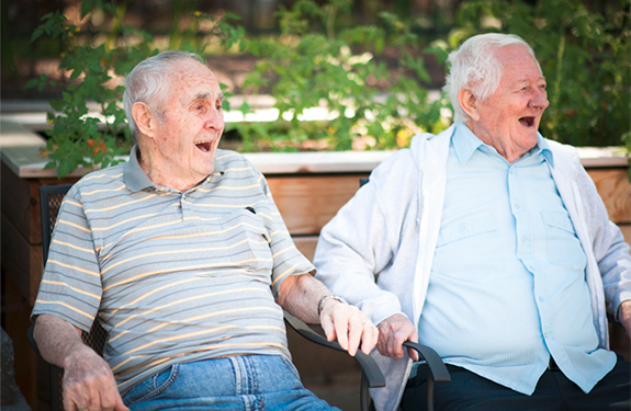 two men sitting on a bench outside laughing