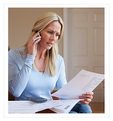 worried woman looking at a piece of paper while making a phone call