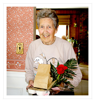 older woman holding a meal and a rose