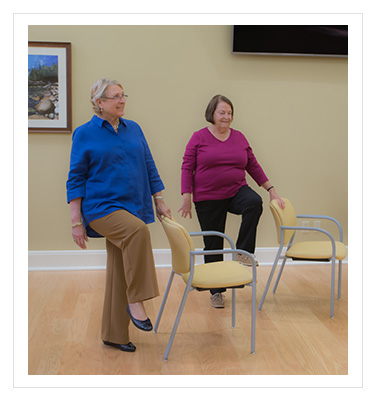 two women performing exercises using a chair for balance