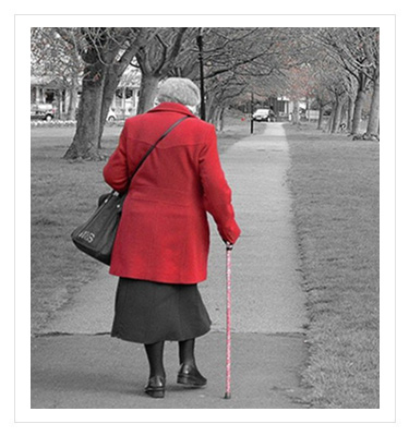 older woman wearing a red coat walking down the sidewalk using a cane